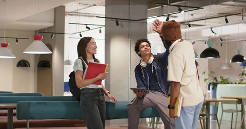 College Students High-Fiving in Modern Campus Lounge Collaborating with Tablet and Notebooks