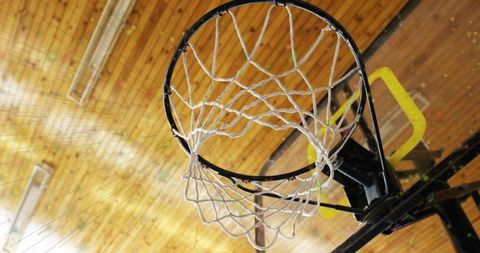 Low-angle basketball hoop hanging with white net and yellow support pad in gymnasium