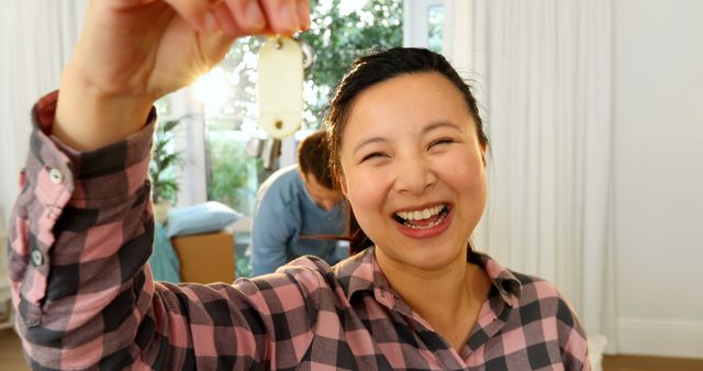 Young woman holding up her new house key, expressing happiness and excitement. Suitable for topics such as home buying, real estate, first-time home ownership, and moving. Also useful for lifestyle imagery illustrating achievement and new beginnings.