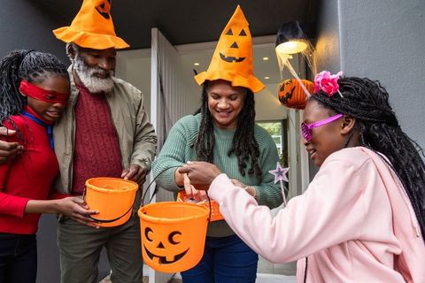 African american family celebrating halloween on porch with pumpkin hats and candy buckets