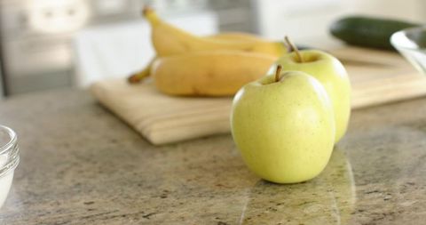 Fresh green apples sitting on granite countertop with bananas and cutting board for healthy snack
