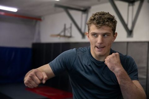 Young male boxer training intense punching drill in indoor gym with padded walls