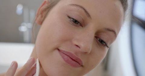 Woman Cleansing Jawline with Cotton Pad in Bathroom