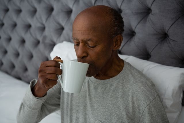 Senior man drinking coffee while sitting on bed at home