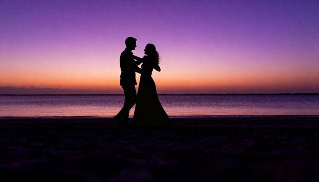 Romantic silhouette couple dancing on beach at purple and orange sunset horizon