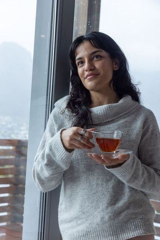 Young Woman Enjoying Tranquil Tea Time Indoors by Large Window
