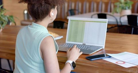 African american woman working on spreadsheet at cafe coworking table with laptop