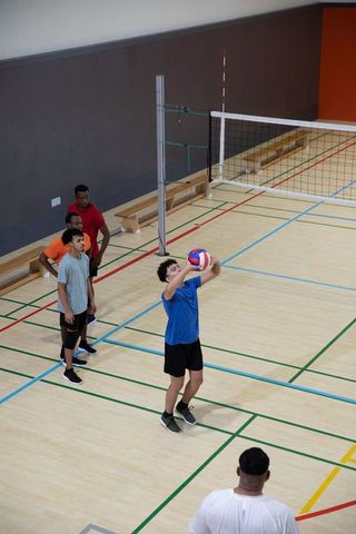 Teen setting volleyball overhead during indoor gym practice with diverse male team