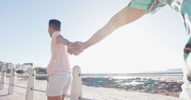 Couple holding hands while walking on a sunny beach promenade - Download Free Stock Images Pikwizard.com