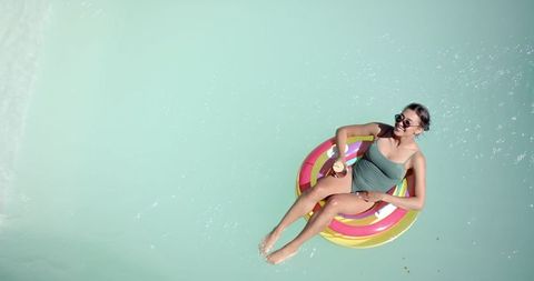 Woman Relaxing on Inflatable Ring in Pool with Beverage