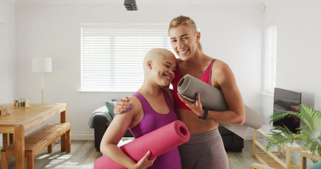 Portrait of happy diverse female couple with yoga mats in living room. spending quality time at home.
