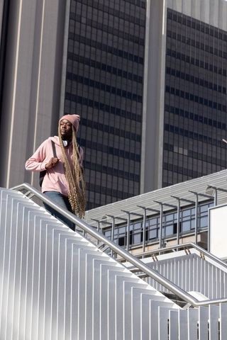 Young african american woman standing on urban metal staircase with backpack and headphones