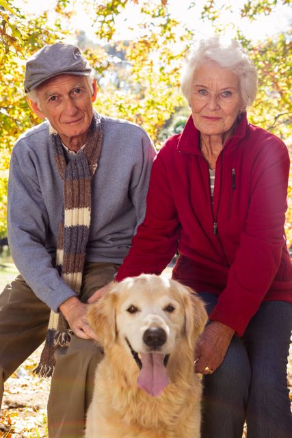 An elderly couple are sitting and smiling at camera with dog in a park 