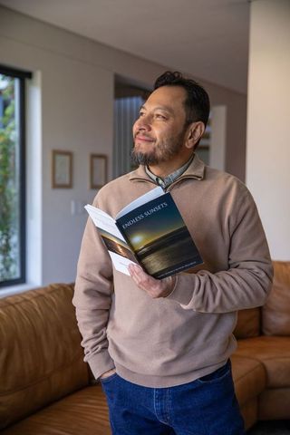 Mature asian man reading endless sunsets and gazing out window in cozy living room