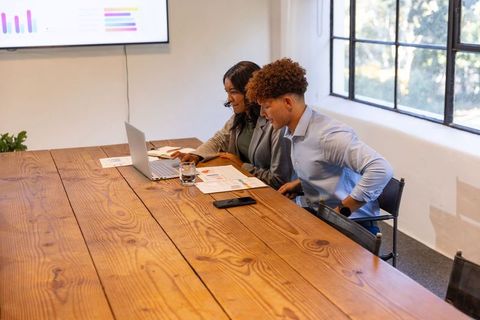 Diverse colleagues collaborating over charts and laptop in bright conference room