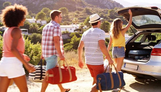 Young friends walking to hatchback and loading luggage on sunny summer road trip