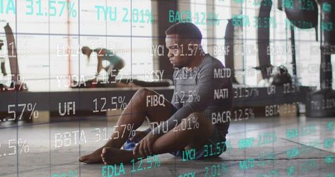 Athlete resting and tending foot on gym mat with financial data overlay, recovery concept