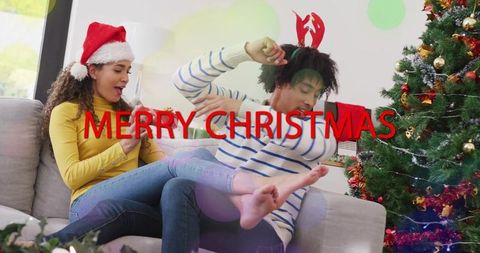 Couple exchanging christmas gift on couch wearing santa hat and reindeer antlers