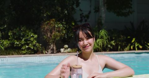 Asian Woman Relaxing by Backyard Pool with Water Bottle