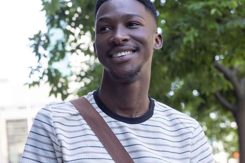 African man smiling outdoors wearing striped sweater and brown shoulder strap urban portrait happy