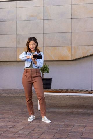 African woman standing in urban plaza holding smartphone horizontally checking smartwatch