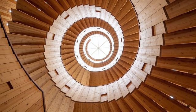 Spiraling wooden staircase drawing gaze upward toward skylight in circular tower