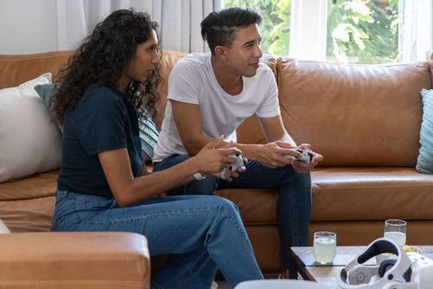 African american couple playing video games on leather sofa in cozy living room
