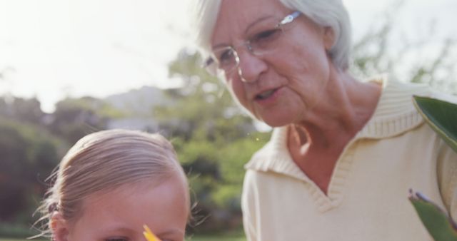 A senior Caucasian woman is sharing a moment with a young girl outdoors, with copy space. Their close interaction suggests a familial bond, a grandmother with her granddaughter.
