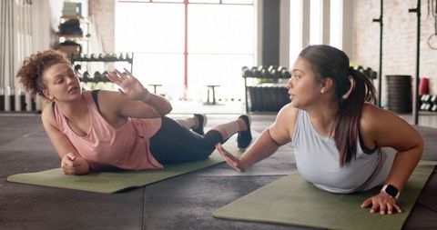 Diverse women stretching and reaching on mats in gym supporting teamwork and wellness
