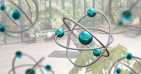 Woman practicing yoga twist in tropical studio with teal orbital sculptures and plants