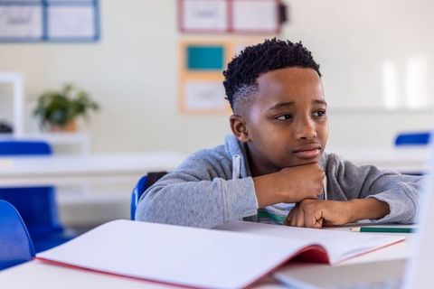 Preteen african american boy resting chin, gazing thoughtfully at notebook in classroom