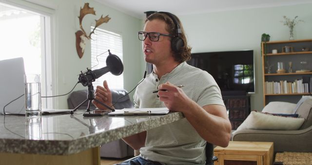 Man recording podcast in modern home studio, wearing glasses and headphones. Suitable for projects related to podcast creation, home office setups, remote working, modern technology, and media production.