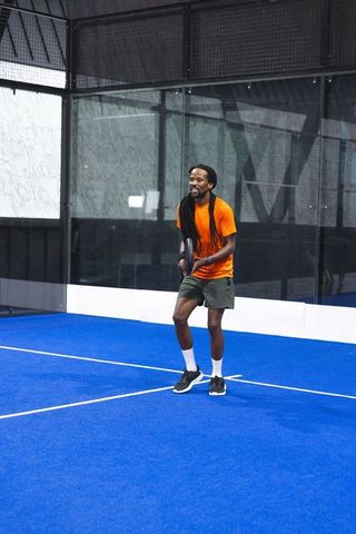 Athletic Man in Orange Shirt Enthusiastically Playing Padel on Blue Court