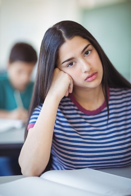 Portrait of sad schoolgirl sitting in classroom at school
