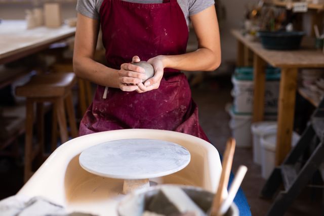 Caucasian female potter holding a ball of clay, shaping it. small creative business at pottery studio.