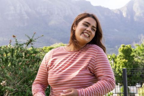 African american woman smiling and enjoying outdoor mountain park in pink striped shirt