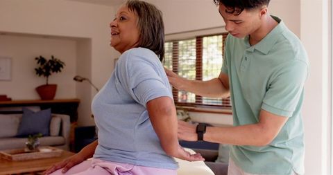 Physiotherapist Assisting Senior Woman with Back Exercises at Home