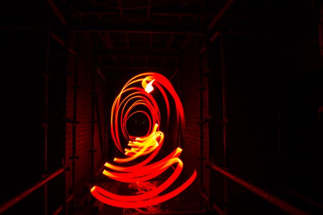 This captivating long exposure shot captures vividly red light trails forming abstract patterns in a dark tunnel. Perfect for use in creative projects, science fiction or futuristic themes, illustrating concepts of movement or technology, and adding a dynamic visual element to websites or blogs.