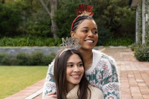 Multiracial friends embracing wearing merry christmas headbands cozy knit sweaters