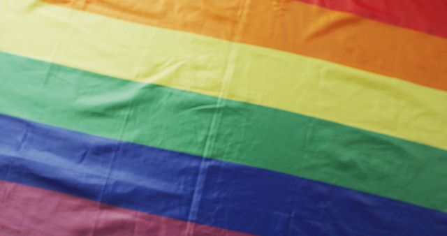 Vivid rainbow flag seen close-up with visible wrinkles symbolizes LGBTQ pride and equality. Useful for celebrating pride events, promoting inclusivity and diversity, or emphasizing social justice and human rights.