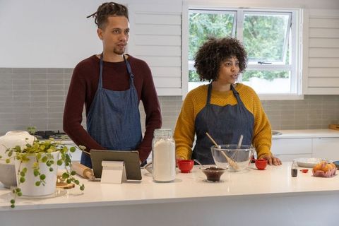 African american couple preparing batter at modern kitchen island wearing denim aprons