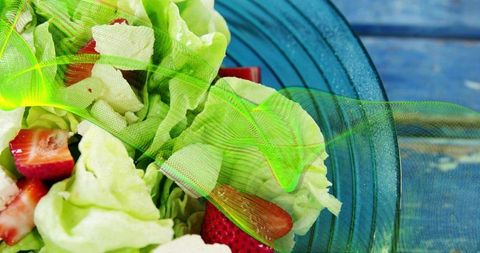 Bright butter lettuce and sliced strawberry salad in blue bowl with lime mesh drape on rustic table