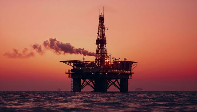 Silhouette of offshore drilling rig at sunset emitting smoke