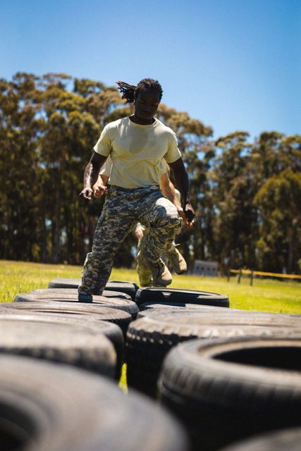 This image captures an African American soldier running through tires during a bootcamp training session. Ideal for use in articles or advertisements related to military training, fitness programs, teamwork, and physical endurance. It can also be used in recruitment campaigns or motivational content highlighting discipline and perseverance.