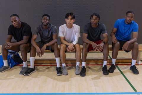 Five male teammates sitting on bench waiting during basketball practice showing focus