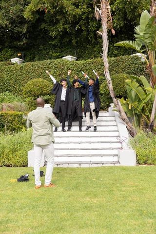 Friends celebrating graduation on garden steps holding diplomas and filming with phone