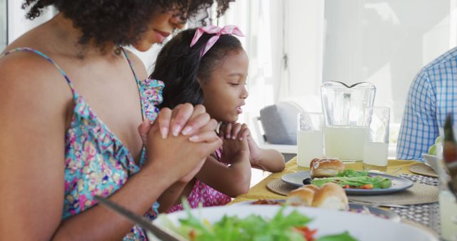 Mother and daughter praying before starting a family meal at home. Ideal for themes related to gratitude, family bonding, faith, and home living. Suitable for articles, publications, and websites focused on family values, religious practices, and healthy lifestyles.