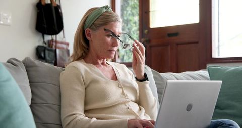 Mature woman using laptop at home while adjusting glasses