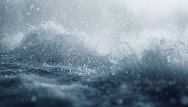 Crashing storm waves sending sea spray across turbulent open ocean under moody light