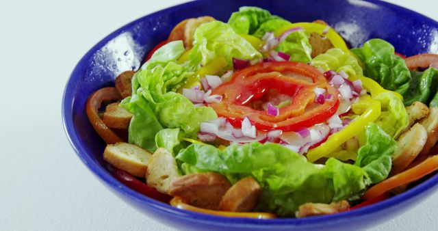 This vibrant vegetable salad featuring lettuce, tomatoes, onions, bell peppers, and croutons in a blue bowl is perfect for promotion of healthy eating, diet menus, vegan and vegetarian recipes, or health and wellness blogs.
